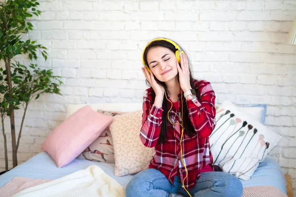 Müzik ve şarkı yatağın üstüne oturan ve cep telefonu tutan kulaklık mutlu güzel kadın