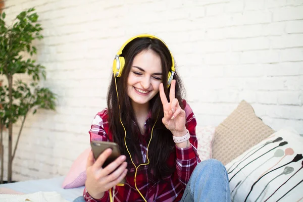 Müzik ve şarkı yatağın üstüne oturan ve cep telefonu tutan kulaklık mutlu güzel kadın