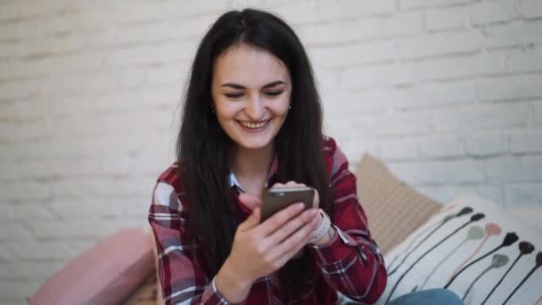 Chica joven sentada en la cama y viendo contenido en el teléfono inteligente — Vídeos de Stock