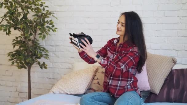 Joven mujer caucásica con gafas de realidad virtual en habitación blanca con árbol verde y cama . — Vídeos de Stock