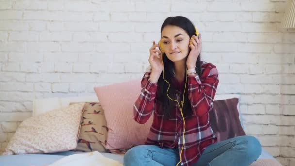 Flickan lyssnar på musik med hörlurar och sitter på sängen Dans — Stockvideo