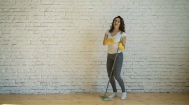 Dans eden bir genç kadın sarı eldivenler güler, bir kadında temizlik tutan bir paspas onun elinde