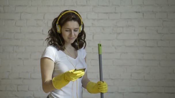 Femme heureuse dans les écouteurs chantant, faisant semblant de MOP le microphone, au milieu du mur de briques blanches — Video