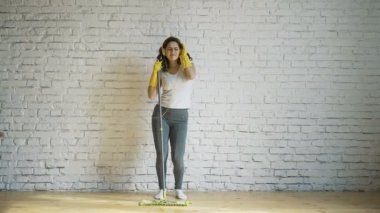 Dans eden bir genç kadın sarı eldivenler güler, bir kadında temizlik tutan bir paspas onun elinde