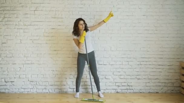Танцующая молодая женщина чистит женщину в желтых перчатках смеется, держит швабру в руках — стоковое видео