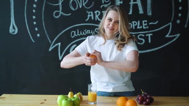 Woman young housewife in the kitchen at home to drink fresh homemade orange juice. Squeeze the juice from the orange. Healthy eating, vegetarian eating, weight loss and people concept — Stock Video