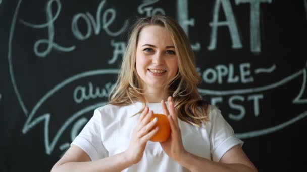 Mulher jovem dona de casa na cozinha em casa para beber suco de laranja caseiro fresco. Esprema o sumo da laranja. Alimentação saudável, alimentação vegetariana, perda de peso e conceito de pessoas — Vídeo de Stock