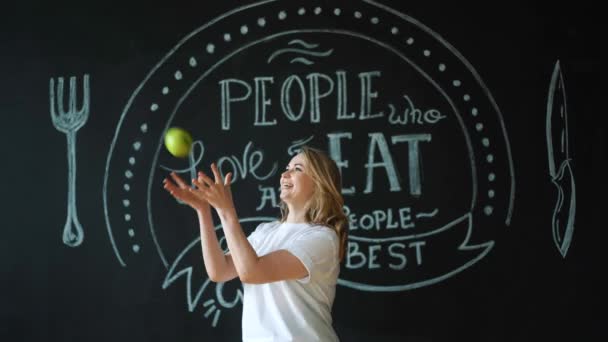 Happy girl fooling around with oranges in the kitchen, juggling, looking at camera. — Stock Video