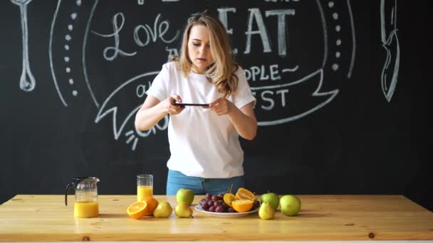 Belle fille caucasienne dans un t-shirt blanc avec chat vidéo, une adolescente joyeuse, pour communiquer via smartphone, prise de vue intérieure dans une cuisine lumineuse et spacieuse avec mur d'ardoise . — Video