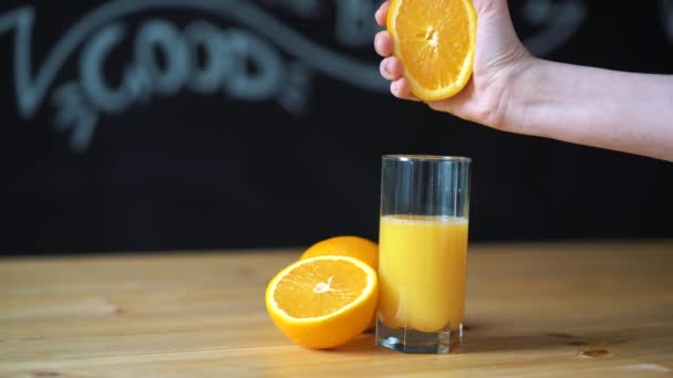 Exprimir a mano el jugo de naranja en transparente, vidrio del vaso. Contra un muro de pizarra negra — Vídeos de Stock