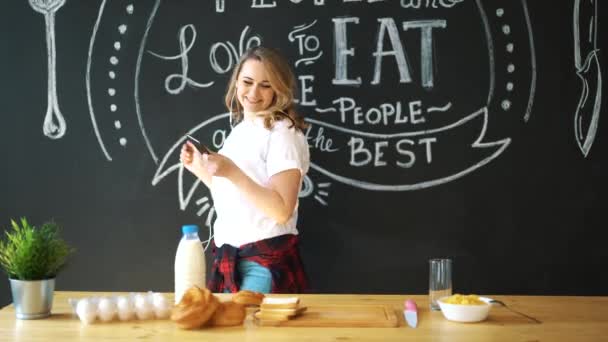 Jovem atraente mulher cozinhar ovos mexidos na cozinha de manhã, sorrindo, feliz dona de casa positiva, estilo de vida saudável, ouvir música em fones de ouvido, rindo, se divertindo, dançando, cantando — Vídeo de Stock