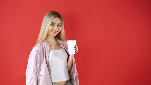 Souriant jeune femme détendue et verre debout et boire du café ramasser sur fond de mur rouge . — Video