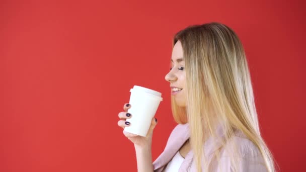 Lächelnd entspannte junge Frau und Glas stehend und Kaffee trinkend auf rotem Wandhintergrund. — Stockvideo