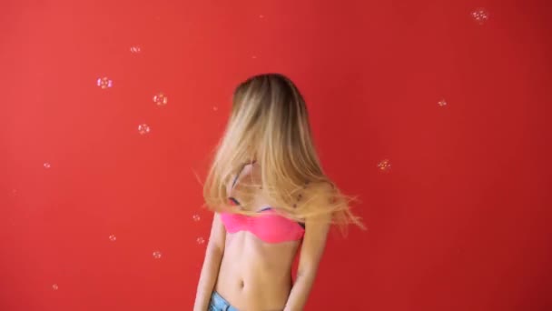 Jolie jeune femme en bikini faisant des bulles de savon isolé sur fond rouge . — Video