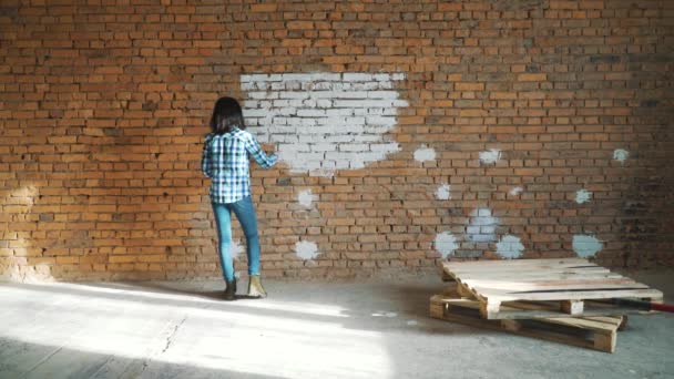 Kvinnan målar ett rött tegel i hus i vit färg — Stockvideo