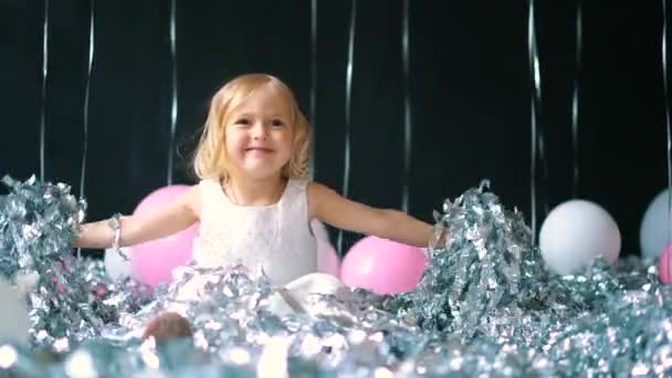 Glad ung flicka i vit glittrande klänning firar med upphöjda händer och leende eller skriker med glädje samtidigt fånga konfetti samtidigt ha roligt — Stockvideo