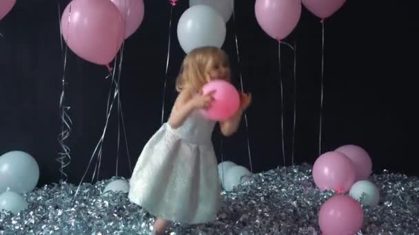 A portrait of a beautiful little girl smiles and holds in a hands color balloon in the studio with many balloons and a toy candy shop. — Stock Video