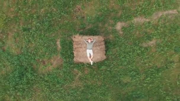 Κορίτσι ξαπλωμένο στα άχυρα σε ένα χωράφι το καλοκαίρι. Εναέρια βίντεο. — Αρχείο Βίντεο