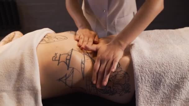 Молодая женщина получает массаж желудка в спа, лежа на массажном столе слайд-долли движения камеры — стоковое видео