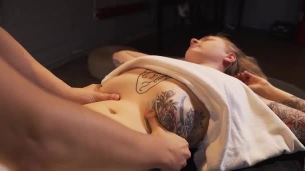 Молода жінка отримує масаж шлунка в спа-салоні, лежить на масажному столі слайд ляльковий рух камери — стокове відео