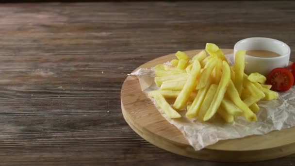 Papas fritas con salsa en un plato de madera, servidas sobre una mesa rústica de madera — Vídeos de Stock