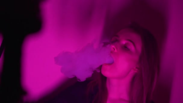 Mooie, jonge, hookah-rokende vrouw. Een aantrekkelijk meisje rookt tabak op smaak. Adem de rook uit in het neonlicht. — Stockvideo