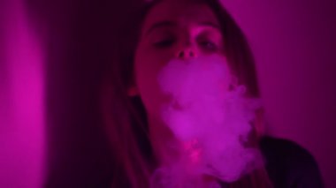 Güzel, genç, nargile tüttüren kadın. Çekici bir kız aromalı tütün içiyor. Dumanı neon ışıkta söndür.