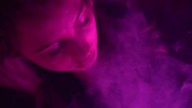 Güzel, genç, nargile tüttüren kadın. Çekici bir kız aromalı tütün içiyor. Dumanı neon ışıkta söndür.