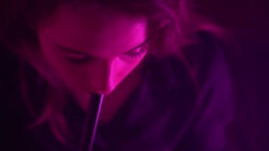 Güzel, genç, nargile tüttüren kadın. Çekici bir kız aromalı tütün içiyor. Dumanı neon ışıkta söndür.