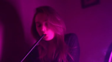 Güzel, genç, nargile tüttüren kadın. Çekici bir kız aromalı tütün içiyor. Dumanı neon ışıkta söndür.