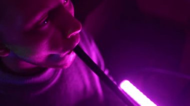 Adam sigara içmek ve neon lambaları yakmak için shisha içiyor..