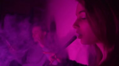 Güzel, genç, nargile tüttüren kadın. Çekici bir kız aromalı tütün içiyor. Dumanı neon ışıkta söndür.