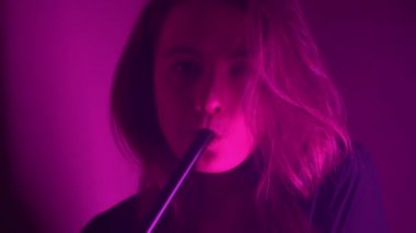 Güzel, genç, nargile tüttüren kadın. Çekici bir kız aromalı tütün içiyor. Dumanı neon ışıkta söndür.
