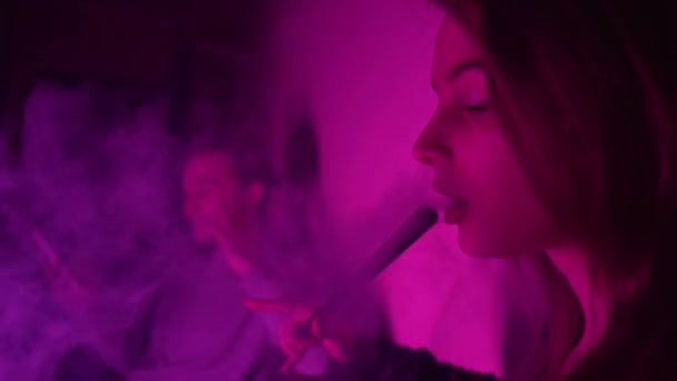 美しく、若い、フカ喫煙女性。魅力的な少女はタバコの風味を吸う。ネオンライトで煙を吹き飛ばせ — ストック動画