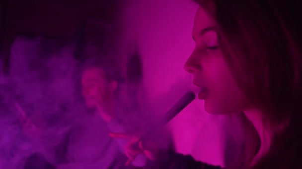 Bella, giovane donna narghilè-fumatori. Una ragazza attraente fuma tabacco aromatizzato. Espirare il fumo nella luce al neon — Video Stock