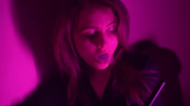 Güzel, genç, nargile tüttüren kadın. Çekici bir kız aromalı tütün içiyor. Dumanı neon ışıkta söndür.