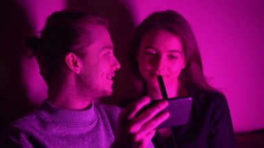 Bir adam ve kız arkadaşı nargile odasında oturmuş telefonlarından video izliyorlar.