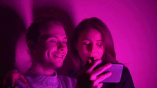 Mężczyzna i jego dziewczyna siedzą w pokoju z dziwkami i oglądają film na telefonie. — Wideo stockowe