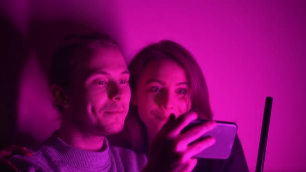 Um homem e sua namorada sentados em uma sala de narguilé assistindo a um vídeo em seu telefone — Vídeo de Stock