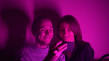 Bir adam ve kız arkadaşı nargile odasında oturmuş telefonlarından video izliyorlar.