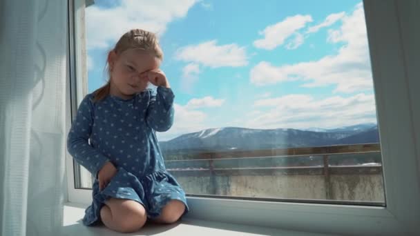 Dziecko jest w domu w izolacji za oknem, płacze i chce się bawić na zewnątrz. Mała dziewczynka uderza w szybę ręką.. — Wideo stockowe