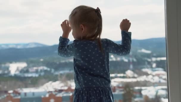 Barnet är hemma i isolering utanför fönstret, gråter och vill leka utomhus. En liten flicka slår i glaset med handen. — Stockvideo