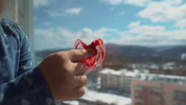 En liten flicka ritar ett hjärta på fönstret med fingret. — Stockvideo