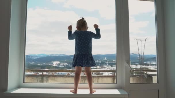 Niña triste mirando por la ventana. Niña aburrida y reflexiva, personas aisladas en cuarentena en casa, brote epidémico de virus, crisis médica . — Vídeo de stock