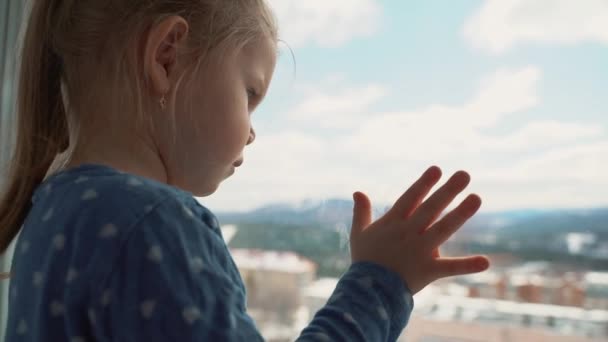 Het kind is thuis in isolatie buiten het raam, huilend en wil buiten spelen. Een klein meisje slaat het glas met haar hand. — Stockvideo