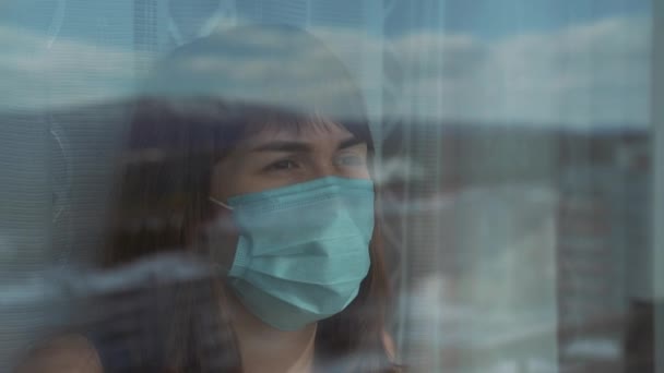 Donna faccia in maschera protettiva blu medica, da vicino. Giovane femmina che indossa una maschera medica per la prevenzione e la protezione delle infezioni virali. Una donna sta davanti ad una finestra dell'ospedale. . — Video Stock