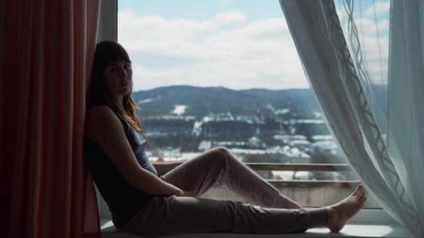 Young woman sitting at windowsill daydreaming looking outdoors natural light. Self-isolation, quarantine — Stock Video