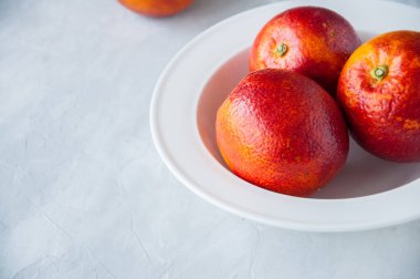 Taze olgun kan portakal beyaz taş zemin üzerine bir tabak içinde.