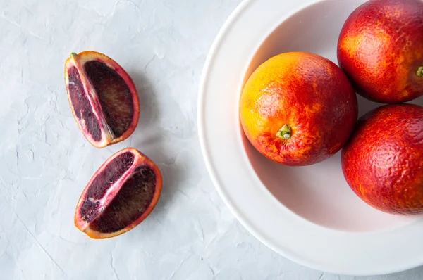 Fresh ripe blood oranges in a plate on a white stone background. — Stock Photo, Image