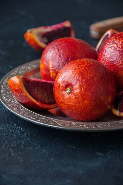 Whole and slices of blood oranges in a vintage plate on a black — Stock Photo, Image